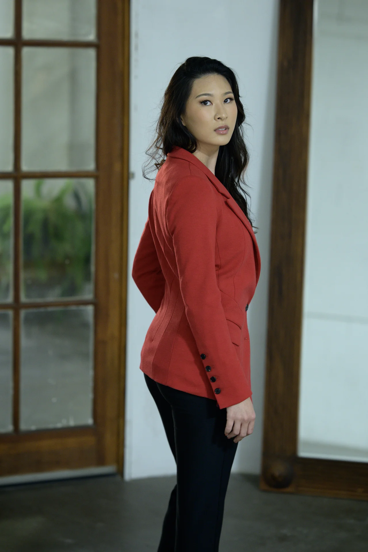 A woman in a red blazer stands in a room with wooden doors and white walls